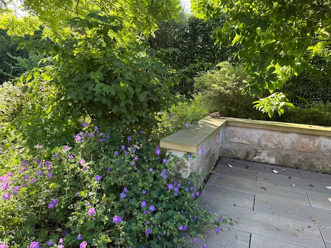 Gemauerte Sitzmauer mit Terrasse und blühender Bepflanzung